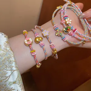 Detailed macro view of hand-woven braided bracelet with enamel flower and gourd charms.
