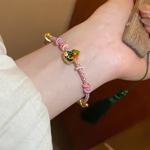 Close-up view of a colorful handmade woven bracelet featuring an enamel flower gourd pendant