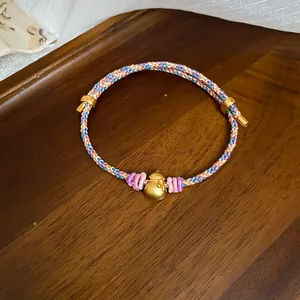 Close-up detail of handmade colorful braided bracelet featuring a golden calabash pendant