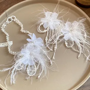 Elegante set di gioielli con fiori di piume bianche e perle di vetro su vassoio beige