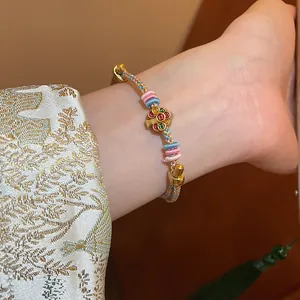 Close-up of hand-woven bracelet with colorful enamel flower pendant on wrist
