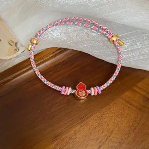Close-up of handmade woven bracelet with red enamel gourd pendant featuring Fu character.