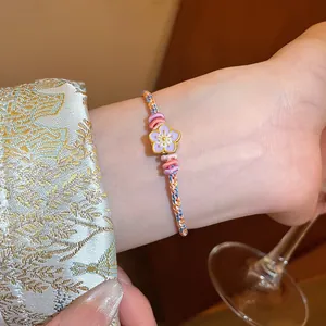 Detail view of a handmade braided bracelet featuring a delicate purple enamel flower charm.