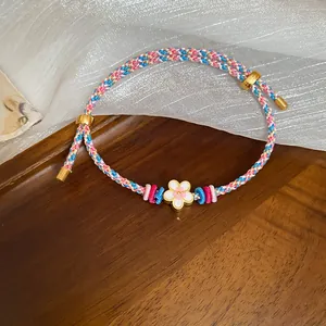 Close-up of a hand-woven colorful bracelet featuring a delicate white enamel flower charm.