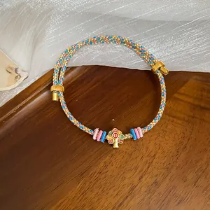 Close-up of a hand-woven colorful cord bracelet with a gold enamel flower pendant.