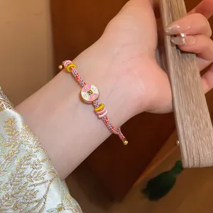 Detailed shot of a hand-woven pink bracelet with an oriental enamel charm on wrist