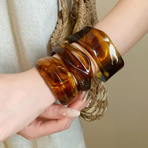 Primo piano di tre bracciali rigidi vintage in acrilico con motivo tartarugato ambra al polso