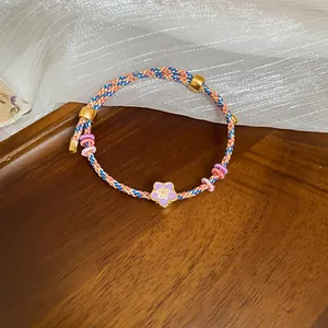 Detailed macro view of a handmade woven fiber bracelet featuring a purple flower oil-dripping pendant