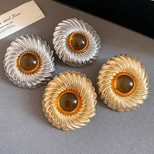 Close-up of gold and silver textured earrings with amber resin centers on a grey surface