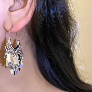 Close-up of silver geometric tassel dangle hoop earrings worn by a model