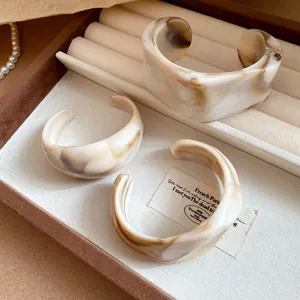 Dettaglio dei grossi bracciali rigidi geometrici in acrilico marmorizzato in un portagioie