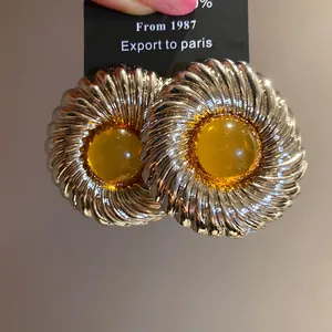 Macro view of silver textured round earrings with yellow resin center detail and ridged design