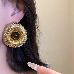 Close-up of vintage gold ribbed round stud earring with green resin center worn on ear