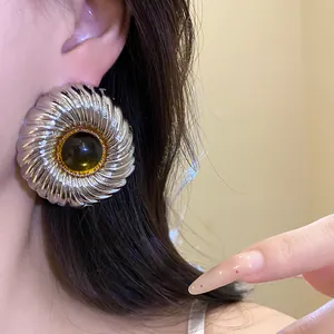 Close-up detail of large silver textured round stud earrings with dark amber resin center