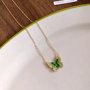 Elegant gold chain necklace featuring a green crystal butterfly pendant on a ceramic plate