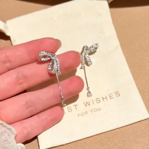 Detailed view of silver bow-knot earrings with zircon-encrusted tassels and teardrop charms