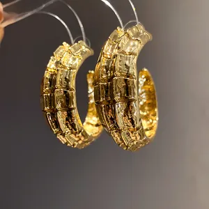 Primer plano de pendientes de aro dorados en forma de C con textura vintage de lujo.