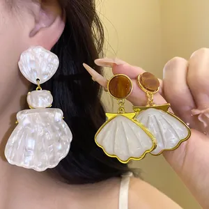 Close-up of vintage shell pendant earrings with pearl-like resin finish and gold trim.