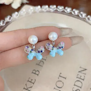 Macro view of blue enamel butterfly earrings with colorful zircon and pearls on silver studs