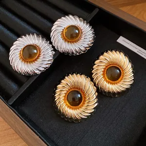 Macro detail of gold and silver textured round stud earrings with amber resin centers