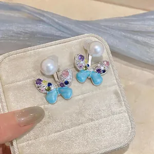 Close-up of butterfly earrings with multi-color zircons and white pearls on velvet box