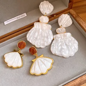 Detailed view of white resin shell earrings with gold accents in a jewelry box.