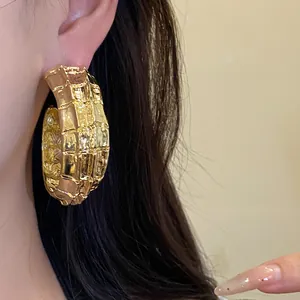 Detalle de un pendiente de aro dorado en forma de C con una textura de pliegues