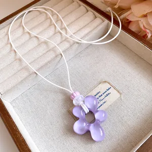 Vista dettagliata di un ciondolo a fiore in resina viola su una collana di cuoio bianco.