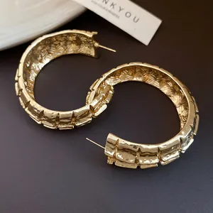 Detalle de elegantes pendientes de aro en forma de C plisados dorados con textura vintage.