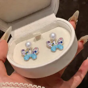 Detailed macro view of colorful butterfly earrings with pearls and blue enamel in a box