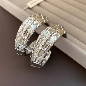 Primer plano detallado de pendientes de aro en C plateados con textura metálica vintage