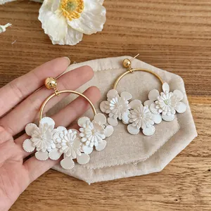 Gros plan d'élégantes créoles dorées avec des fleurs en cuir blanc et perles.