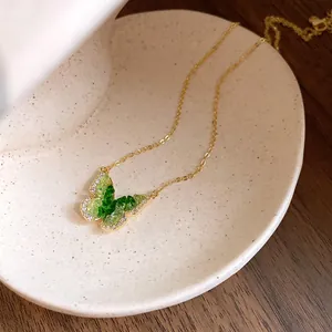 Macro view of a gold chain necklace with a green crystal butterfly pendant