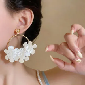 Gros plan d'un mannequin portant d'élégantes créoles avec des fleurs en cuir blanc.