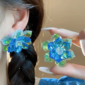 Gros plan détaillé de boucles d'oreilles fleurs en cristal bleu portées à l'oreille et à la main