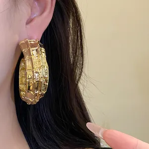 Primer plano de pendientes de aro dorados en forma de C con textura