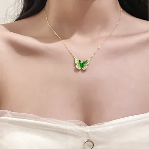 Detail of a gold necklace featuring a green crystal butterfly pendant on a model.