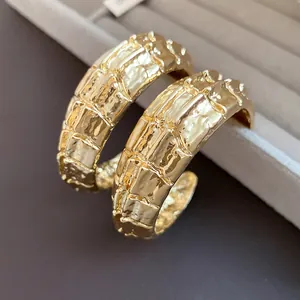 Primer plano de pendientes de aro dorados con textura en forma de C y acabado vintage
