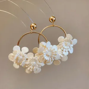 Gros plan détaillé de boucles d'oreilles créoles dorées avec fleurs en cuir blanc et perles