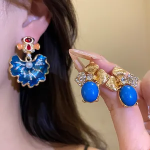 Close-up of vintage enamel leaf earrings with blue stones and sparkling rhinestones.