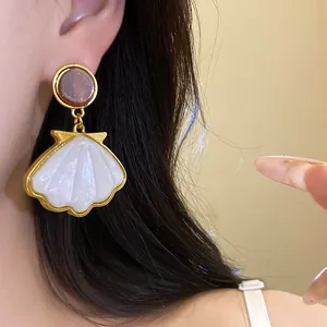 Close-up view of vintage French shell pendant earrings with golden rim worn by a model