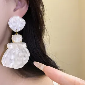 Close-up of white pearlescent resin shell drop earrings worn for vintage French style
