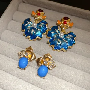 Detail view of vintage enamel goldfish earrings and blue gem studs on a grey tray.