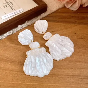 Detailed view of vintage French style white resin shell drop earrings on wood surface