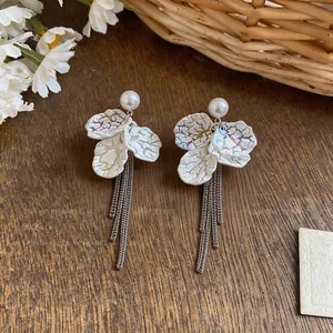 Detailed view of white iridescent petal tassel earrings with pearls on wooden background