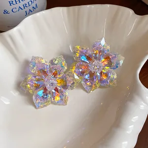 Détail de boucles d'oreilles fleurs en verre iridescent dans un bol en forme de coquillage blanc