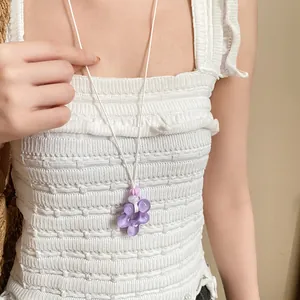 Dettaglio di una dolce collana con ciondolo a fiore in resina viola su top bianco.