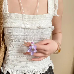 Dettaglio di un ciondolo a fiore in resina viola su una collana a cordoncino bianco.