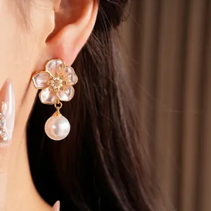 Boucles d'oreilles fleur en émail doré avec une perle blanche pendante sur un mannequin