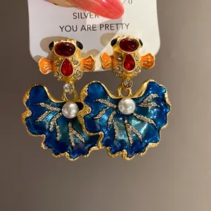 Close-up of vintage blue enamel leaf earrings with red stones and pearl details